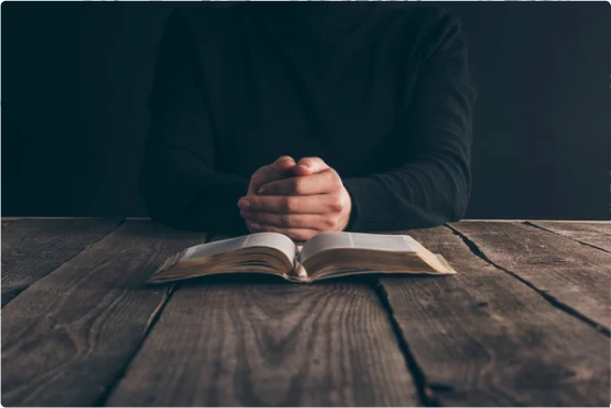 A person with clasped hands reading a Bible.